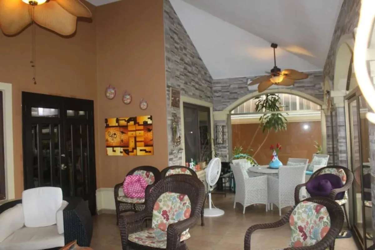 Enclosed patio with stone wall wicker furniture ceiling fans and lush garden view in Sunset Coast Costa Sur