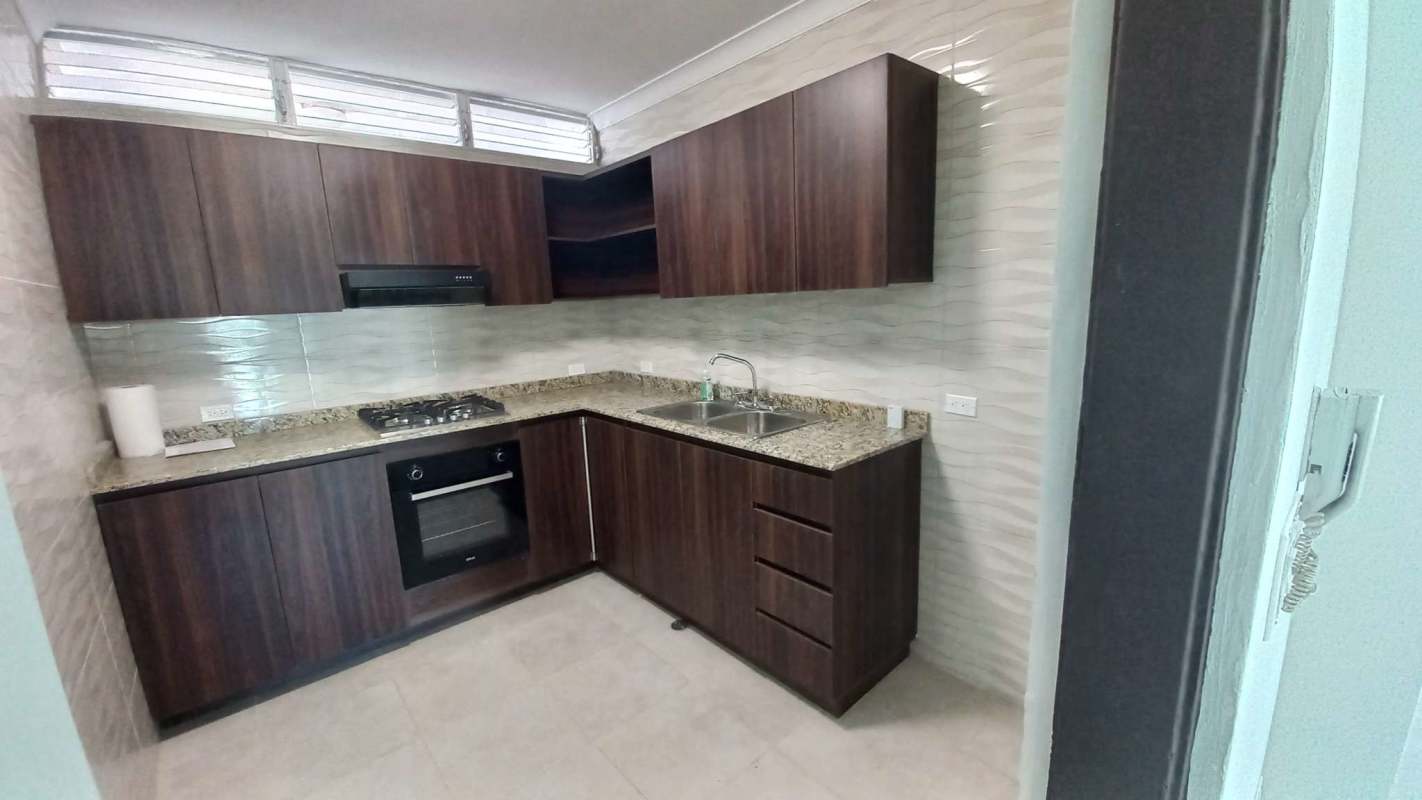 Kitchen with granite countertop, gas stove, built-in oven, vent, dark cabinets in PH Seawaves Obarrio Panama