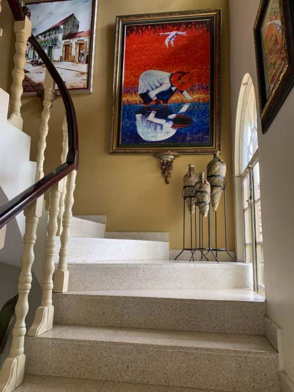 Traditional staircase with wooden handrail, colorful art and large window in Villa de Las Fuentes Panama