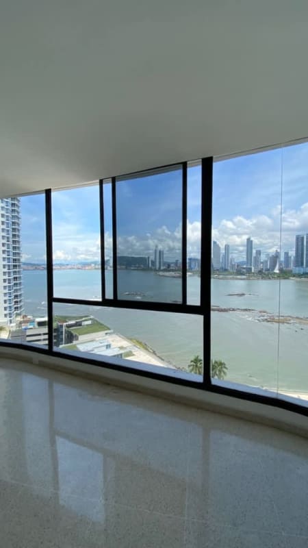 Enclosed sunroom balcony with floor to ceiling windows overlooking city skyline and bay