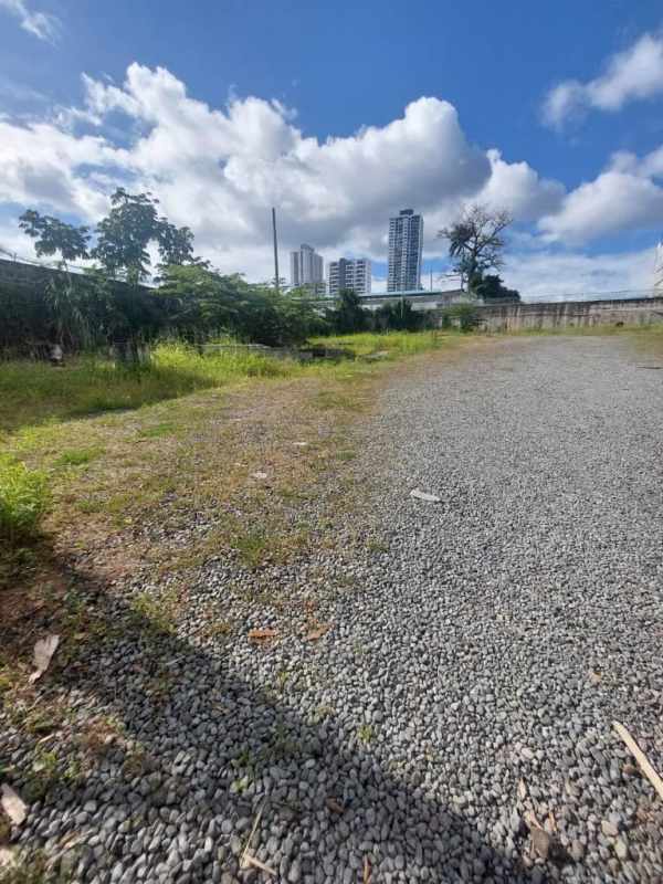 Gravel lot with greenery and city skyline ideal for commercial development