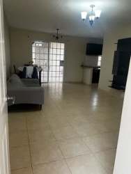 Living room with entertainment unit, beige tile, open to kitchen in Playa Leona rental house Panama
