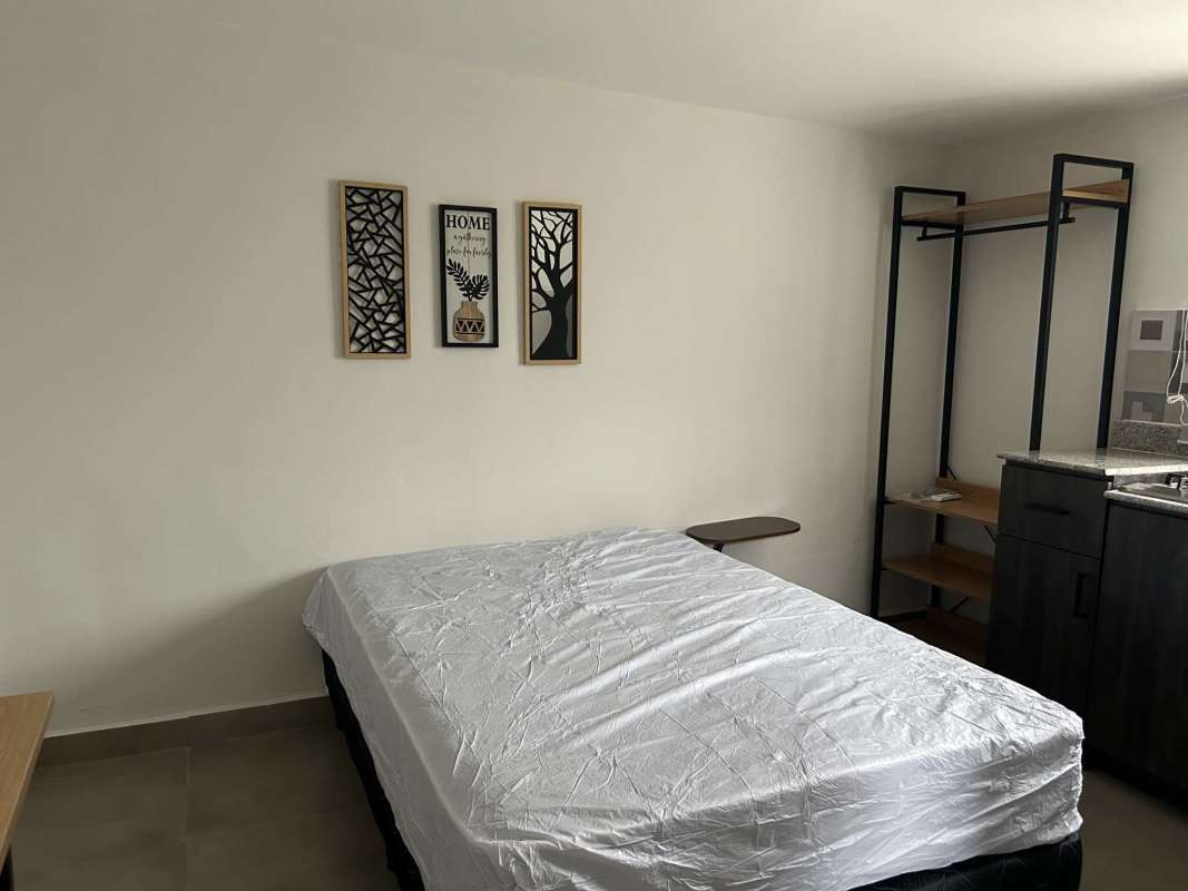 Minimalist bedroom area with open wardrobe, granite counter and wall art in studio rental Tocumen Panama