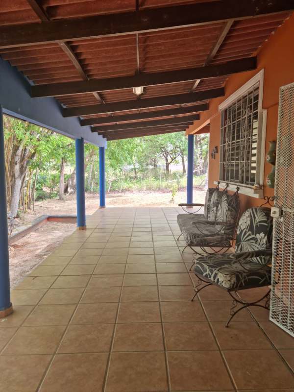 Covered porch with floor tiles, blue columns, and metal chairs overlooking garden Chilibre Panama