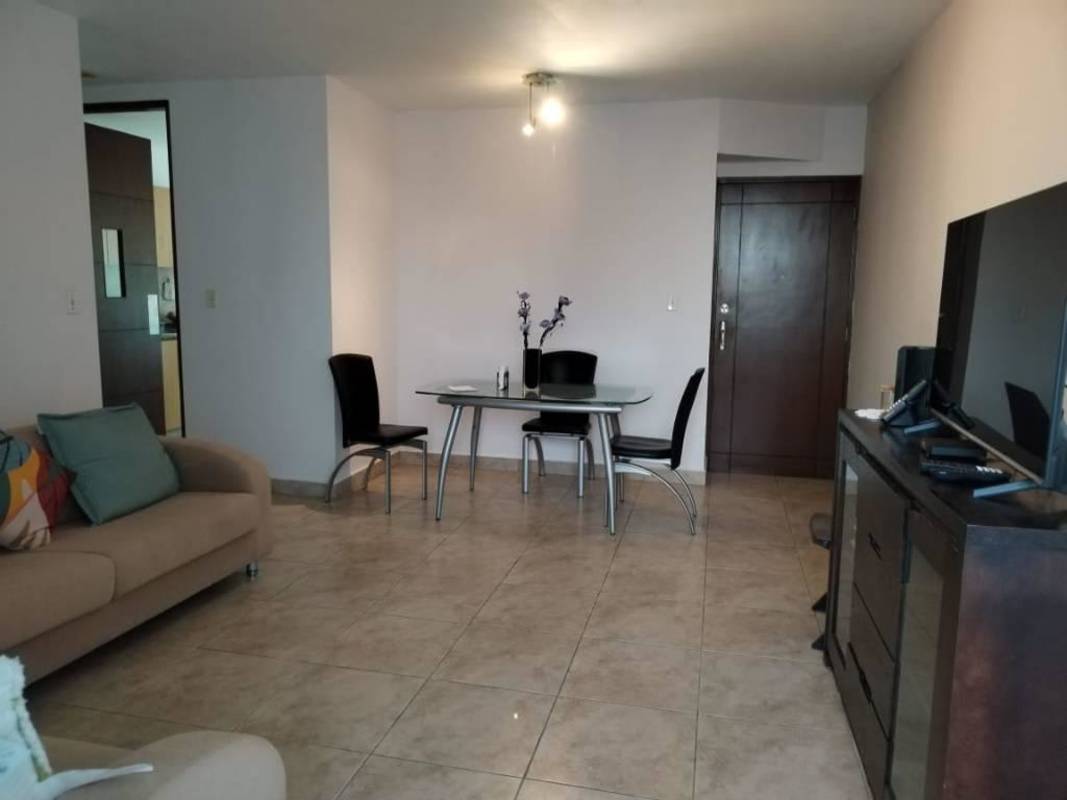 Living space with sofas, glass dining table, TV and large windows overlooking city skyline PH Vista Tower El Cangrejo