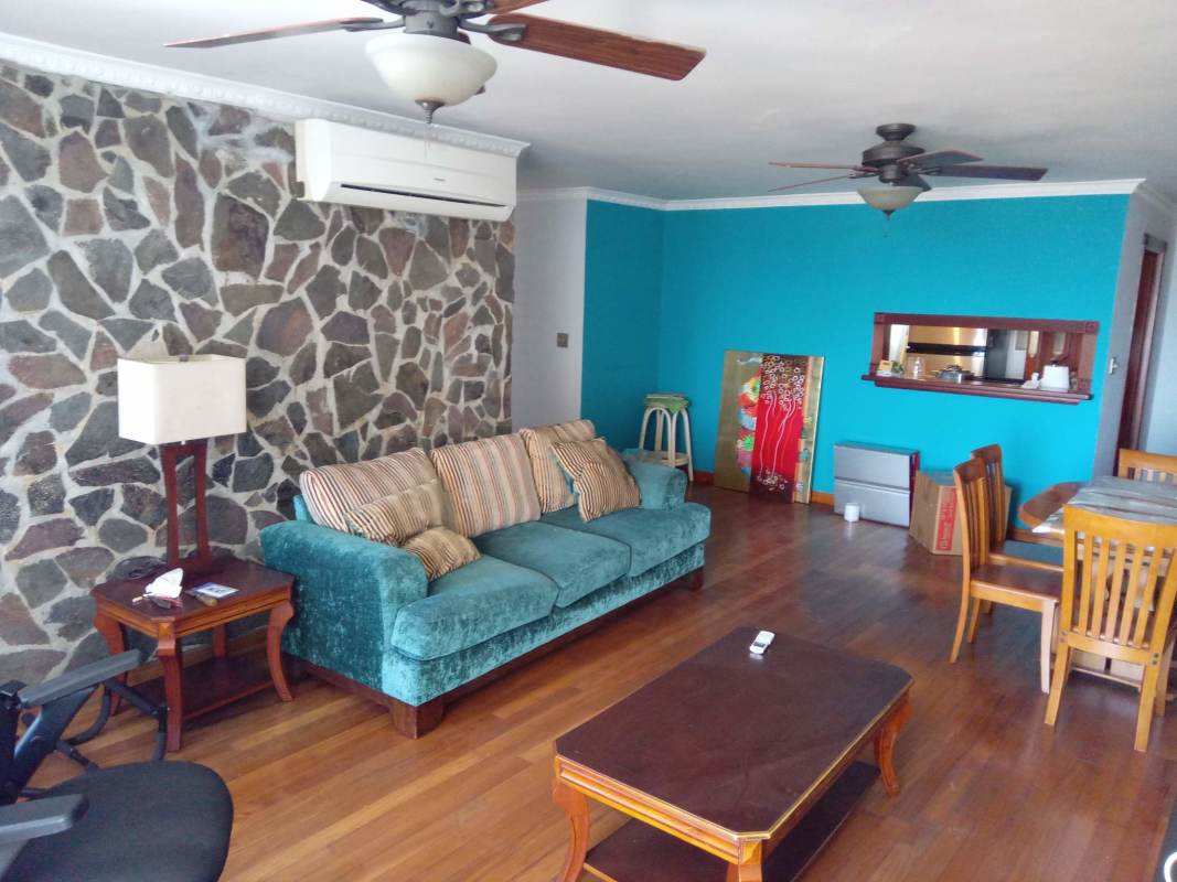 Living room with stone accent wall, teal sofa, wood floors in PH Park View II Panama