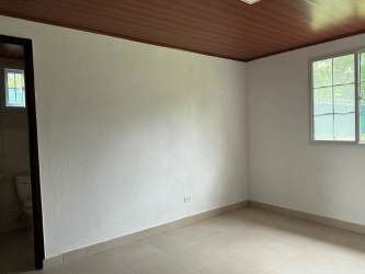 Rustic yellow country house front view with covered porch on large grassy lot in San Carlos Panama