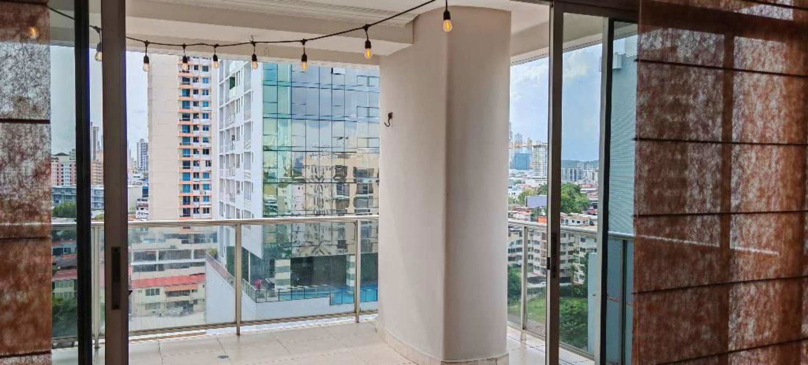 Covered balcony with glass railing string lights overlooking city PH Fairmont Plaza Panama City
