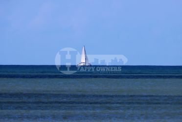 Distant sailboat over calm blue Pacific in front of Búcaro Los Santos land parcel