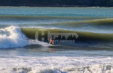 Surfer riding waves near beachfront land in Bucaro Panama with ocean backdrop