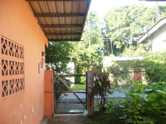 Entrance gate fenced with orange wall, lush plants, metal awning in Panama house