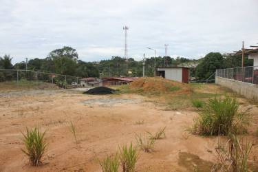 Open plot with patchy grass, utility poles nearby, chain link fence, ideal for new construction