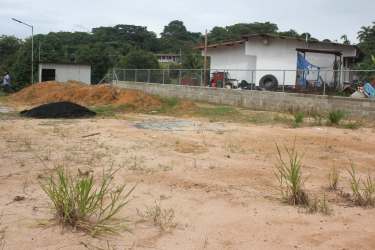 Flat dirt-surfaced corner lot fenced, surrounded by neighborhood housing Puerto Pilón Panama