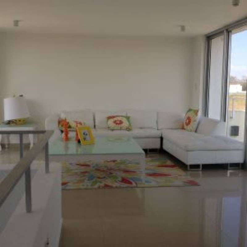 Bright modern living room with large windows, natural light, and tile floors in Costa Sur home