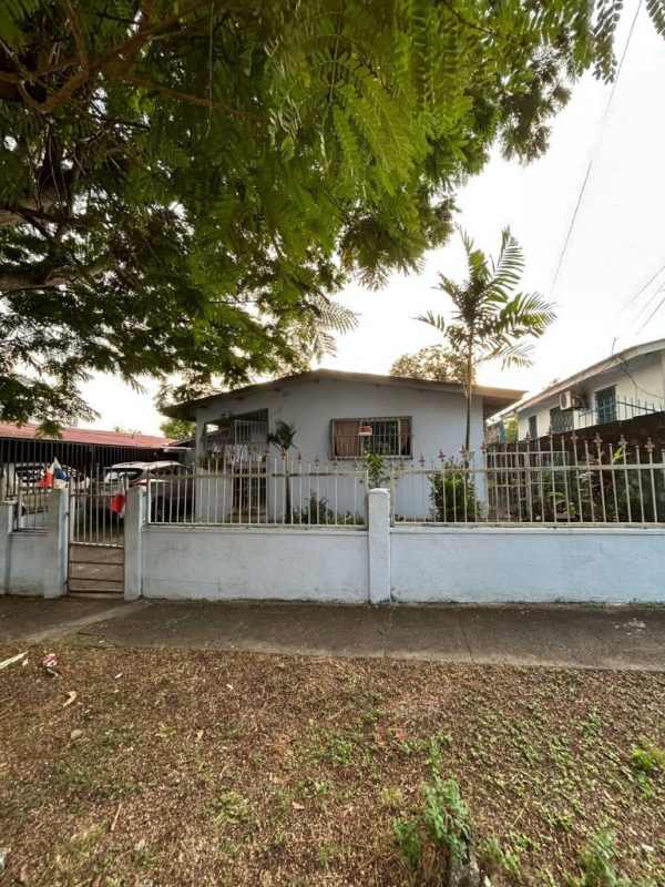 Single-story light blue house, gated fenced yard, palm tree, and carport in Villa Cáceres Panama
