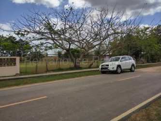 Flat grassy lot near main highway with fencing and natural surroundings