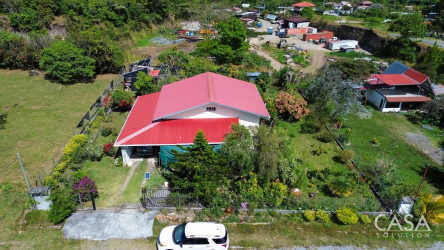 Aerial view of single-story house with red roof, fenced yard, lot and mountain scenery in Boquete Panama