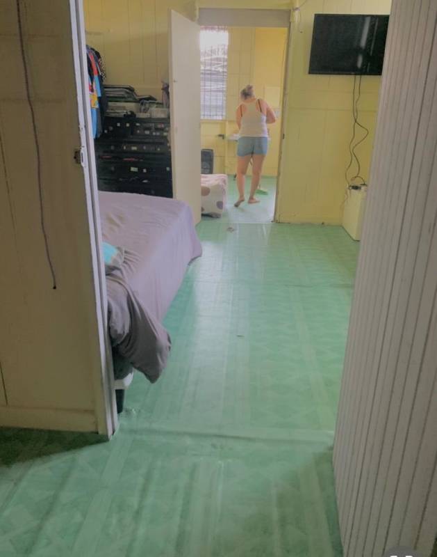 Simple bedroom space with green floor, wood walls, TV, and view into bathroom studio rental Llano Bonito Don Bosco Panama