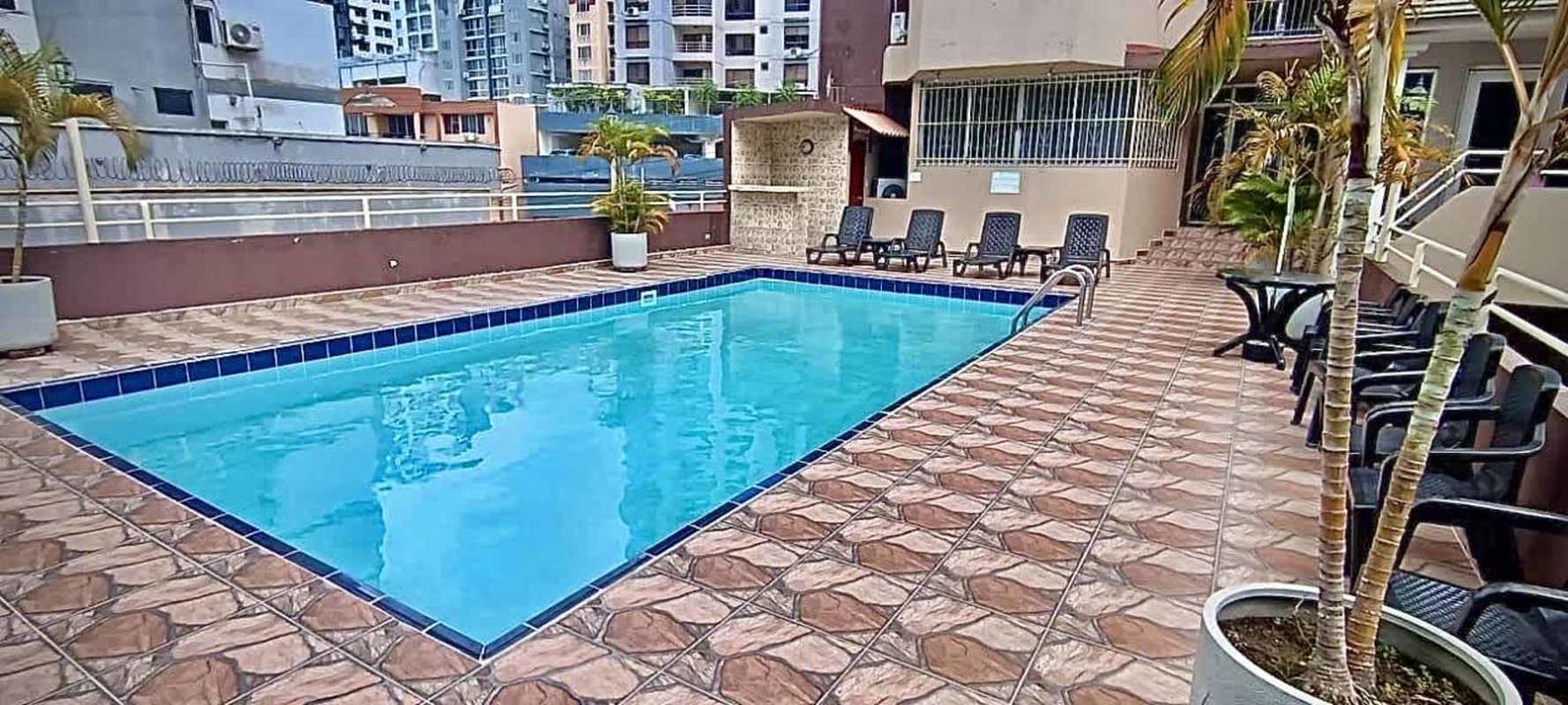 Outdoor shared swimming pool area with sun deck, lounge chairs and city backdrop at Villa de las Fuentes Tower