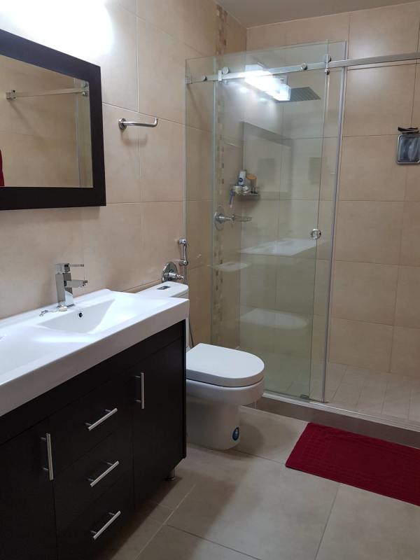 Modern bathroom with glass enclosure, vanity cabinet and beige tiles at Embassy Village