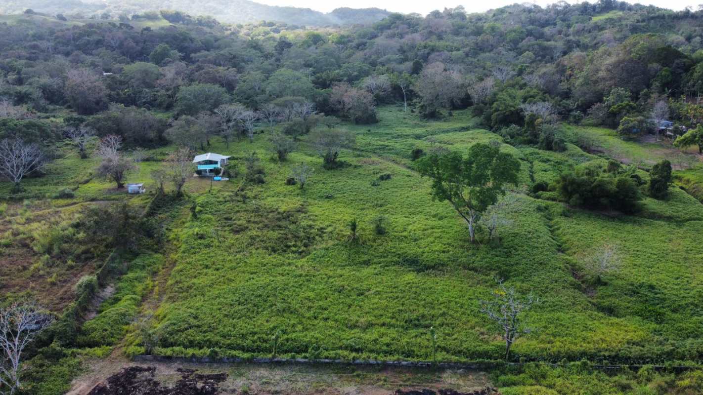 Lush hills and a small white-roof home near forest adjacent to sizeable investment lot in Panama