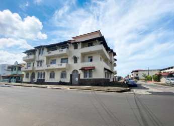 Street corner angle showing La Riviera apartment building with balconies and red awnings for sale