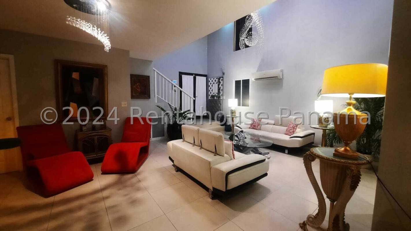 Glass enclosed balcony with wicker furniture, ceiling fan, and panoramic skyline view at night in Panama