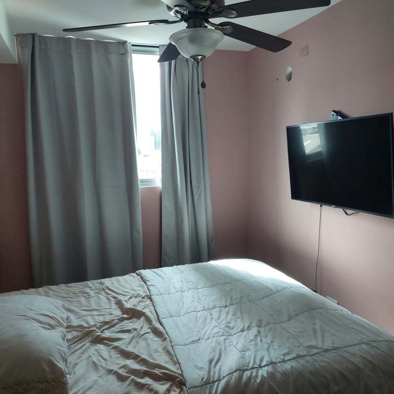 Compact bedroom with pink accent wall, window, wall-mounted TV and AC in Panama apartment