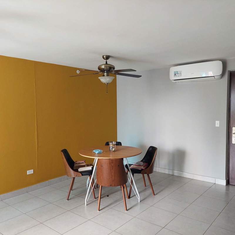 Dining room with yellow accent wall, round table, ceiling fan, AC in Panama apartment