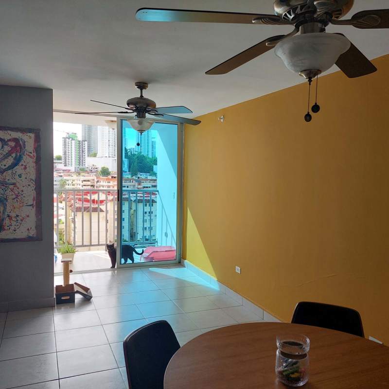 Dining space with ceiling fan, yellow accent wall, sliding balcony doors in apartment behind Parque Omar Panama