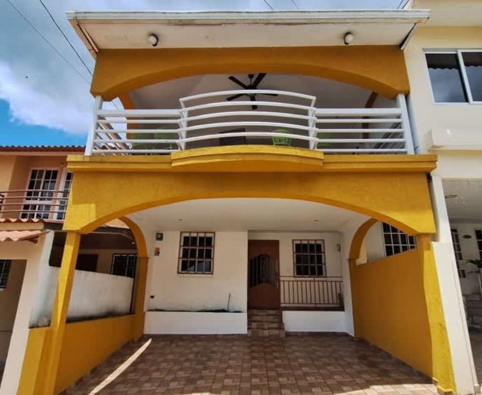 Two-story yellow duplex with arched entrance, tiled carport and balcony at PH Villas del Naranjal Pedregal Panama