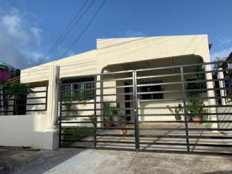 Beige single-story house with metal fence, covered porch and garden plants in Panama Oeste