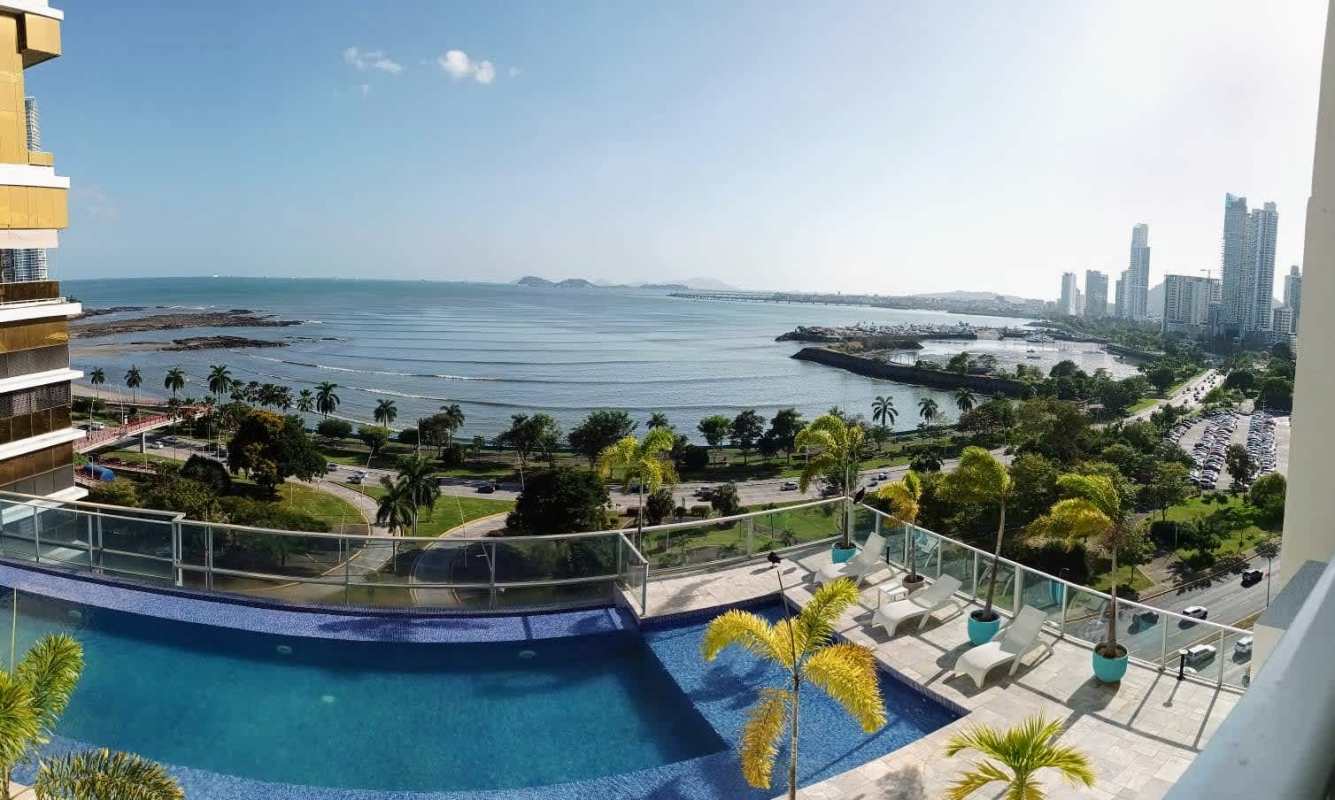 Open living area with floor-to-ceiling glass doors opening to balcony with ocean view in luxury Panama condo