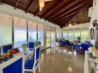 Open living & dining room with glass windows, wood ceilings, and blue furniture in luxury beach house.
