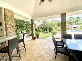 Covered patio lounge and dining space with pool and garden views in Punta Barco home