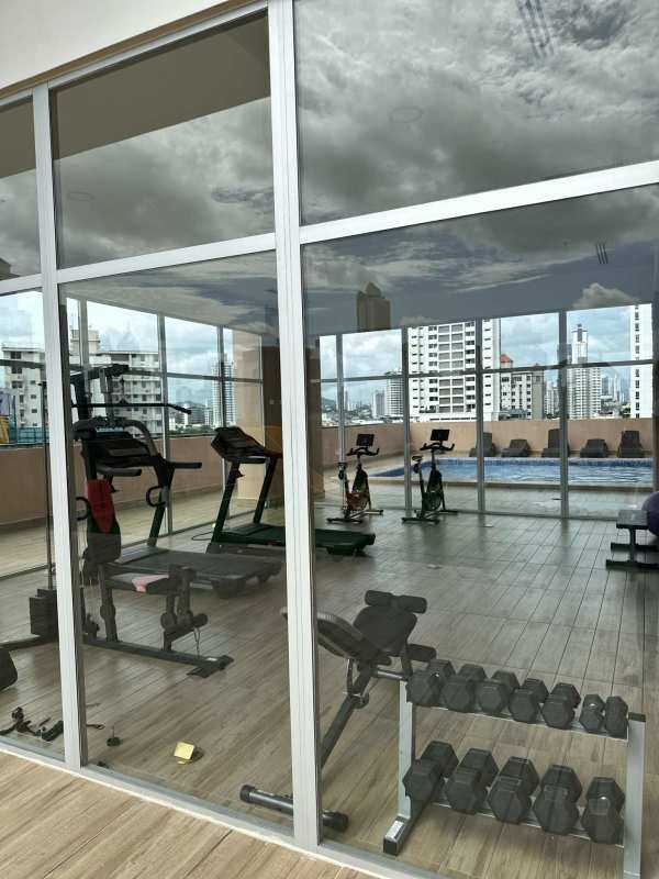 Modern gym with glass wall overlooking rooftop pool at PH Vicky Village Panama City