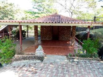 Stone-walled outdoor covered patio with tile roof surrounded by garden plants near river