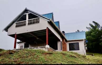 Rural home with blue roof, balcony and porch on grassy lot in Panama mountains
