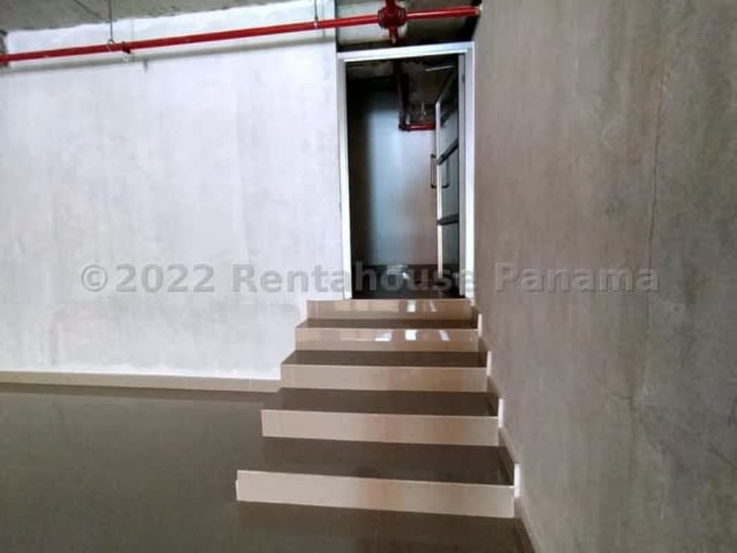 Raw industrial corridor with floating stairs and exposed ceiling pipes in Pueblo Nuevo