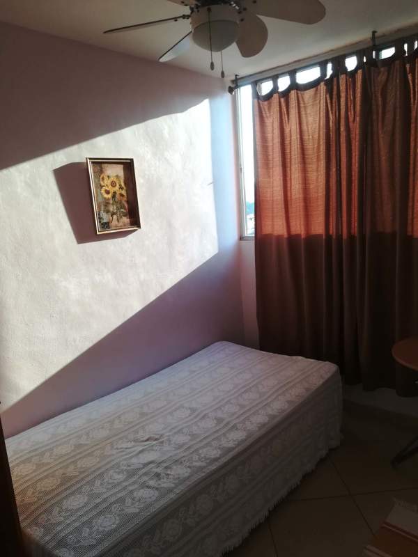Small bedroom with fan, curtains, sunflower painting, and single bed at PH La Cresta Residences in Panama City