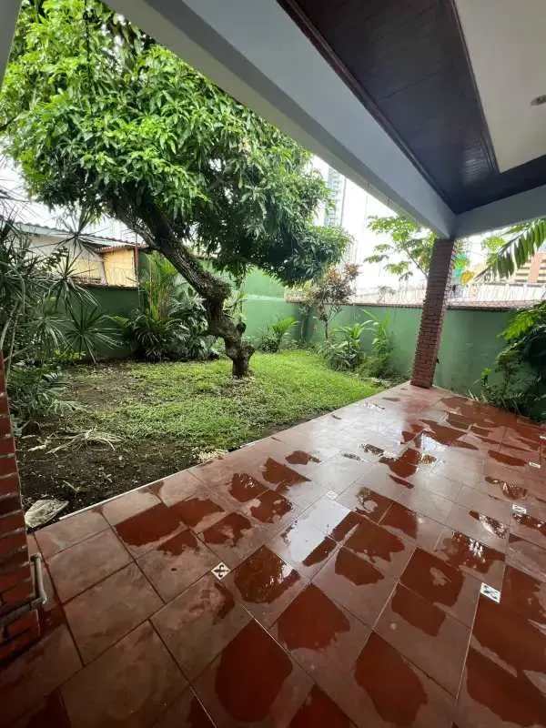 Covered terrace with red tiles and lush green garden in San Francisco Panama house