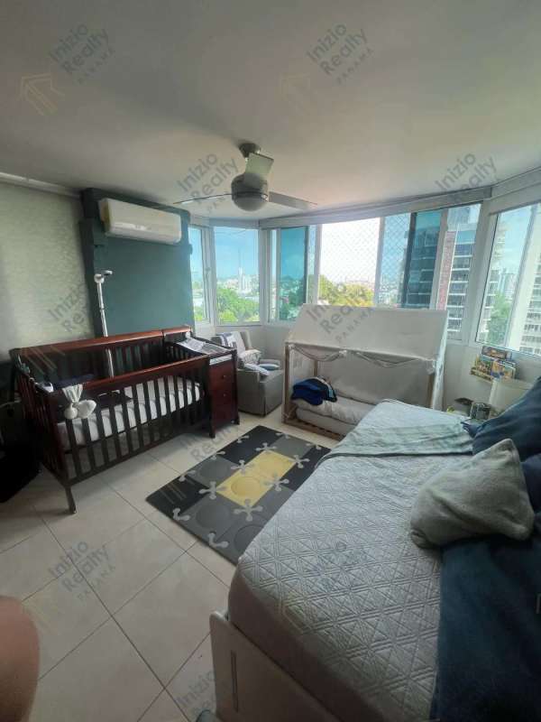 Modern bedroom with large windows, ceiling fan, split AC, crib, and city views in El Cangrejo apartment