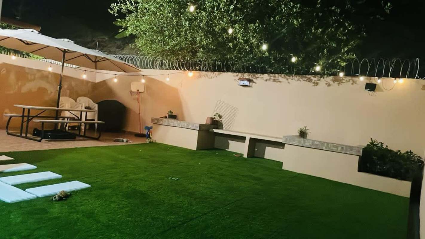 Backyard patio with artificial grass, string lights, picnic table, planters, night ambience Villa Lucre Panama home