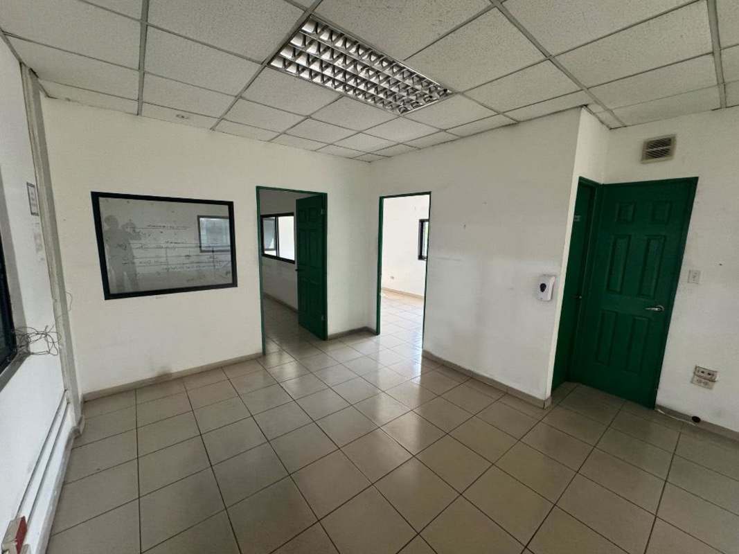 Empty commercial office area with tiled floors, fluorescent ceiling lights, green doors in warehouse Panama