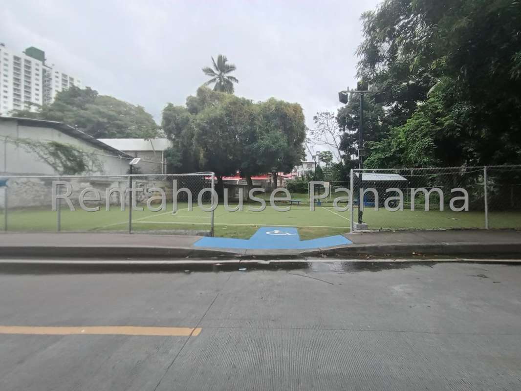 Urban grassy area with pavilion, mature trees, benches inside fenced lot Carrasquilla Panama