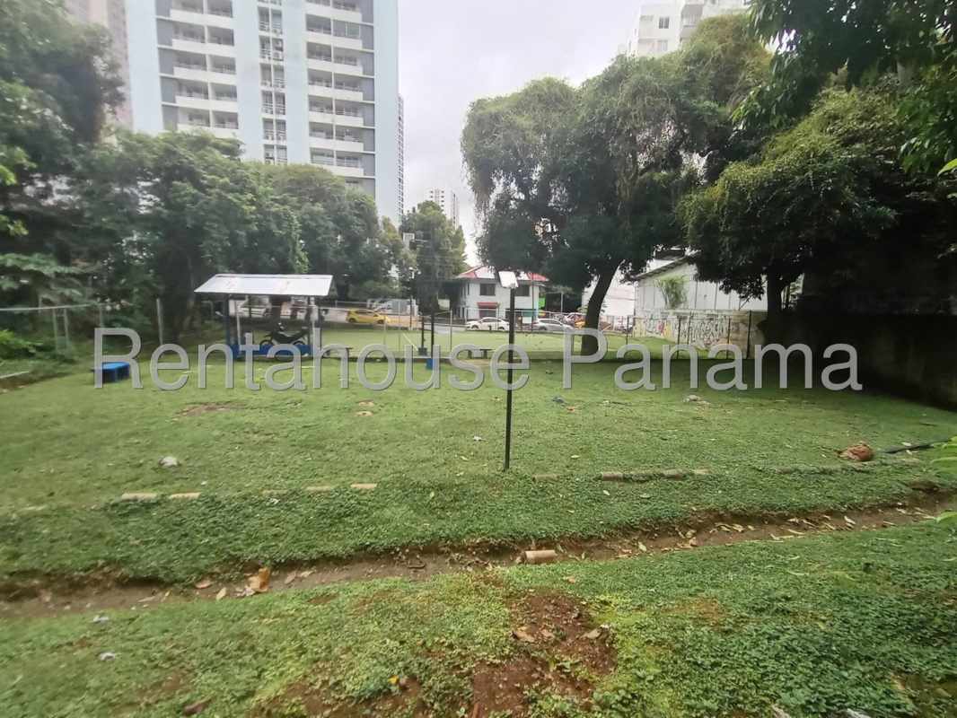 Grassy outdoor area with tall trees and covered seating pavilion in Carrasquilla Panama