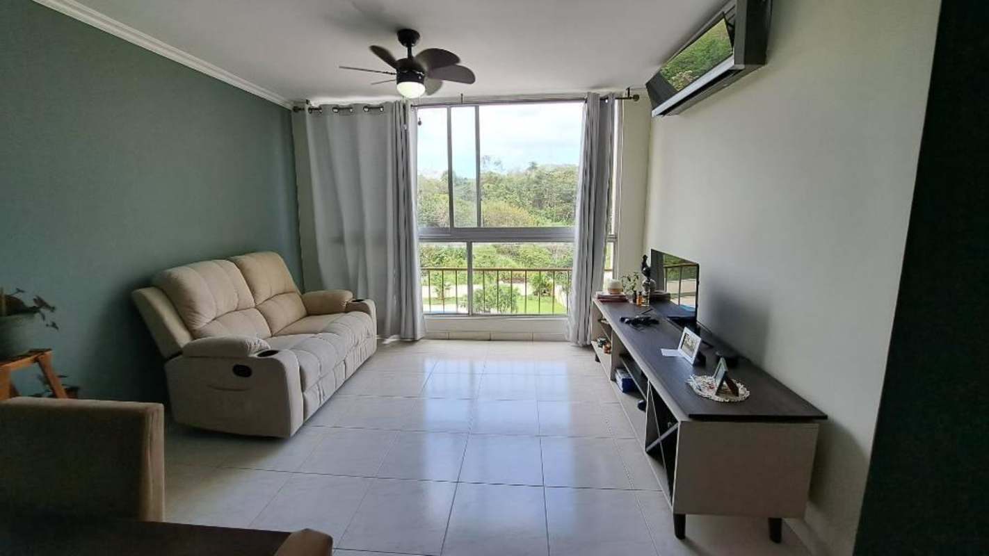 Living room with large window, sofa, TV console, and greenery views in PH Mc Gregor Valley Panama City