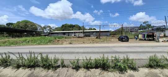 Vacant fenced commercial plot beside road with nearby parked vehicles in El Espino Panama