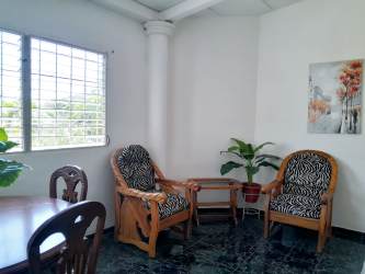 Cozy living dining room with wood chairs, plants, window with bars in duplex rental Chitré