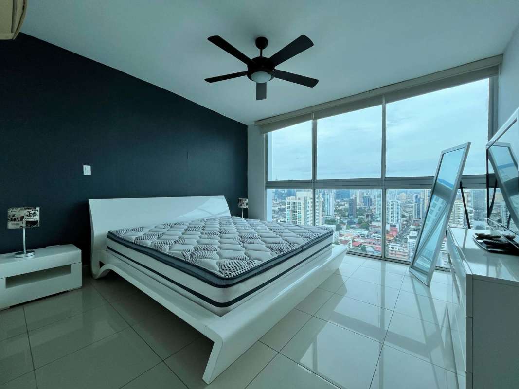 Modern bedroom with large windows, city view, and minimalist furnishings in PH Titanium San Francisco Panama